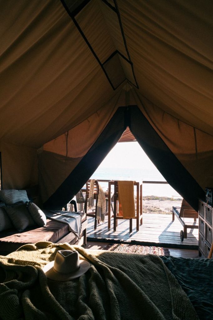 Interior of big tent with beds and lounges outside against sparkling water of sea on beach
